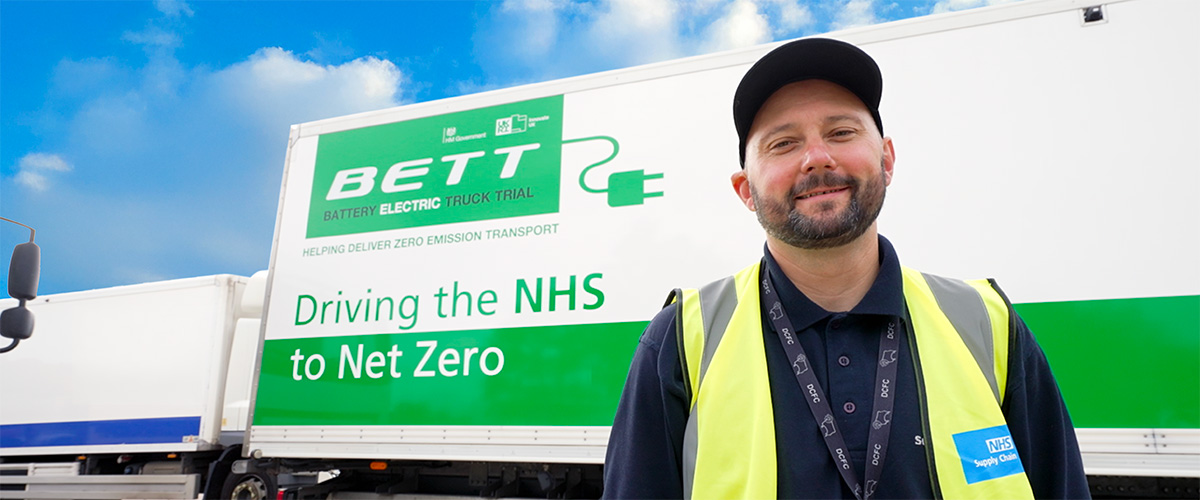Driver with an electric lorry displaying the text "Driving the NHS to Net Zero" A driver with a lorry with the message "Driving the NHS to Net Zero"