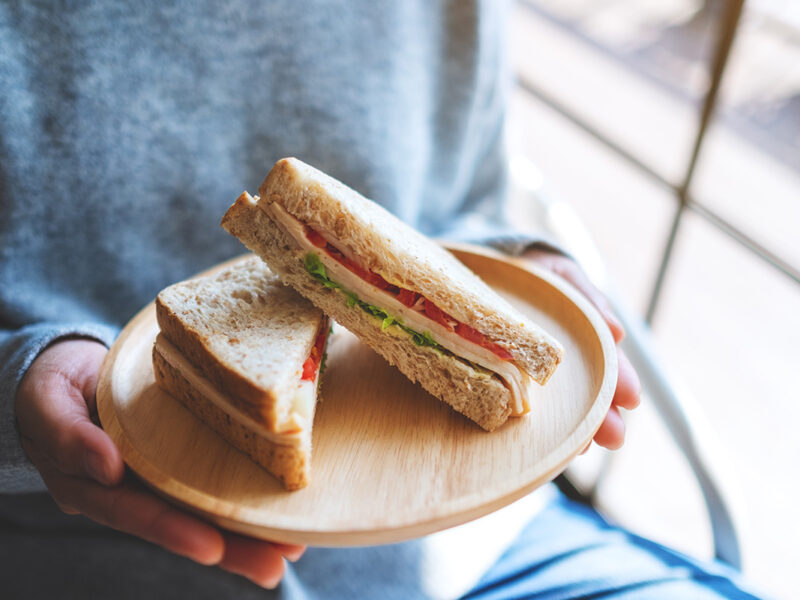 A person holds a tomato, chicken and lettuce sandwich on a plate