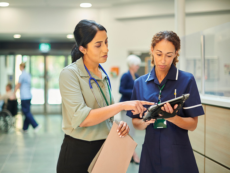 Clinicians looking at tablet in hospital hallway.