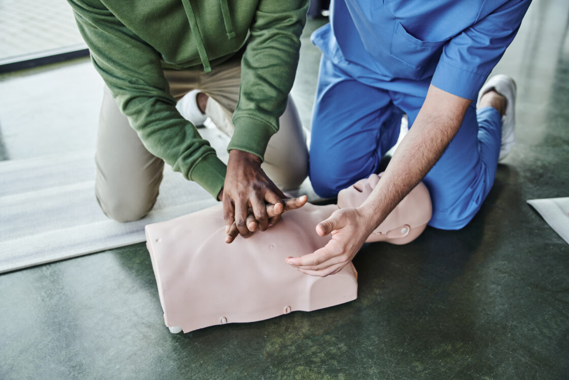 Man being guided on how to perform chest compressions on rescue manikin