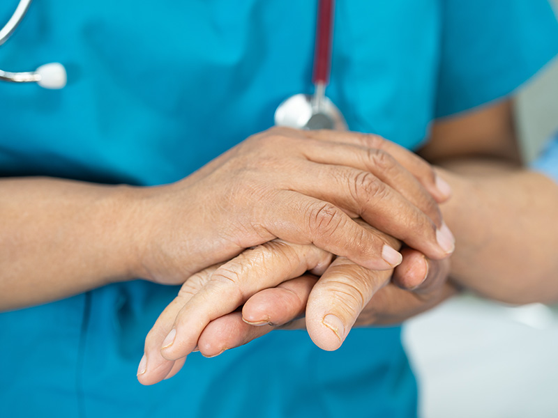 Close-up of a healthcare professional in blue scrubs holding a patient’s hand
