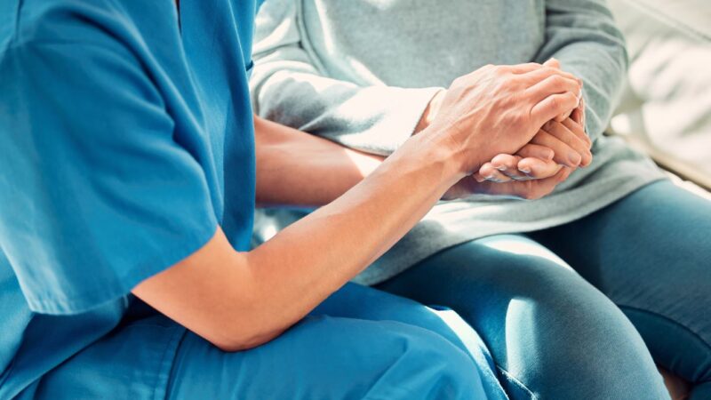 Nurse with patient holding hands providing support in healthcare environment
